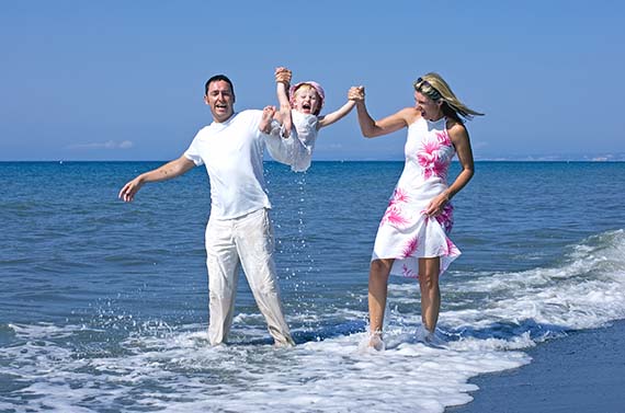 young, happy family playing with daughter in sea on beach in spain whilst on vacation