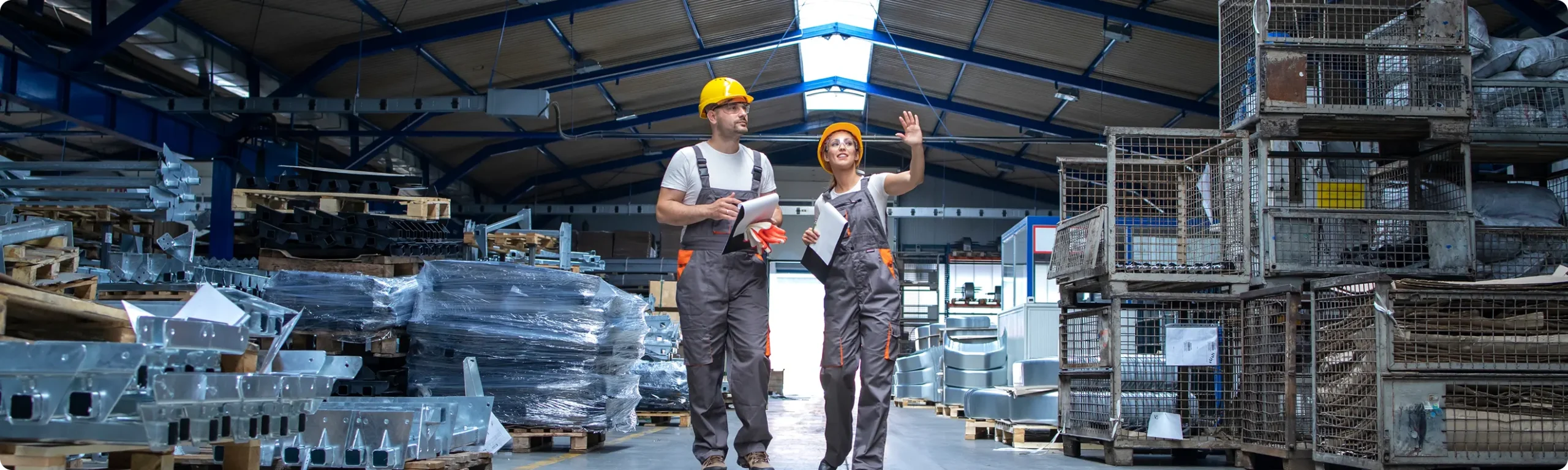 2 people wearing hard hats walking through warehouse