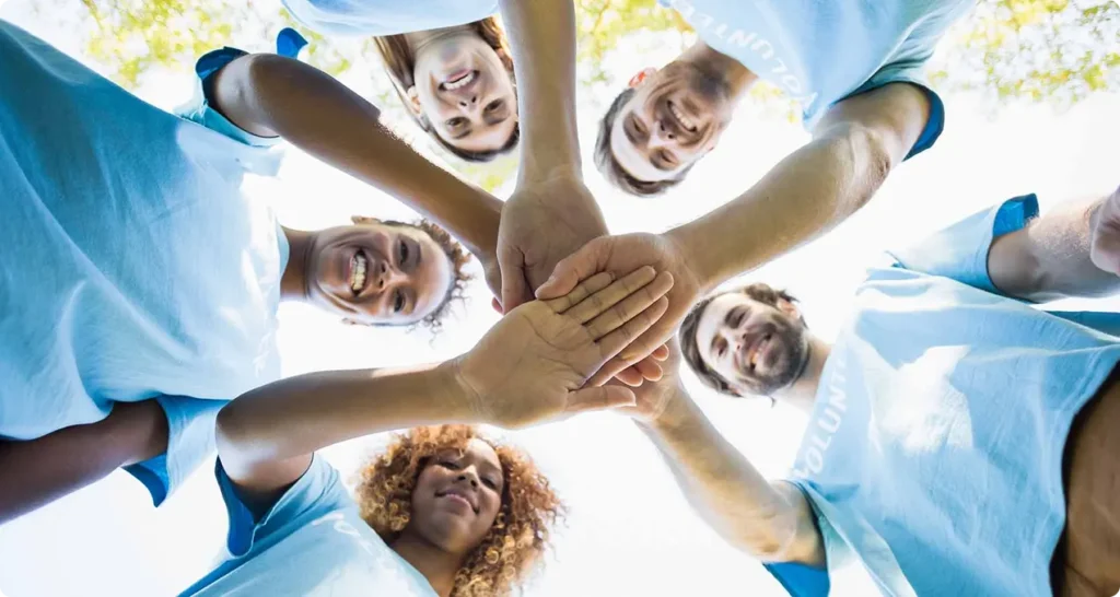 5 people standing in circle with their hands in the center
