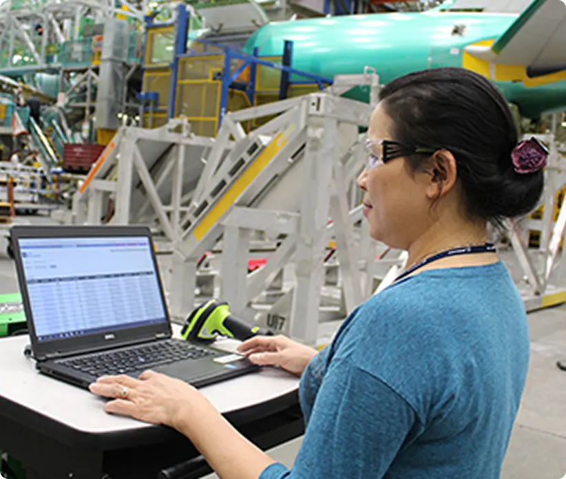 woman wearing safety glasses working on a laptop in a warehouse